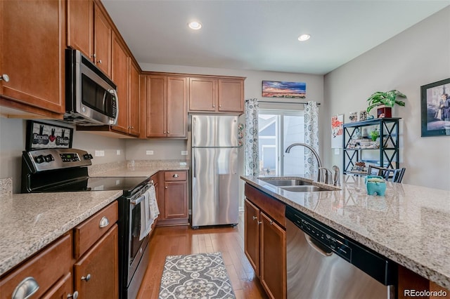 kitchen with light wood-style flooring, appliances with stainless steel finishes, brown cabinets, light stone countertops, and a sink