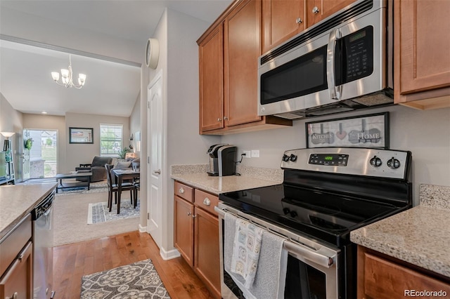 kitchen featuring a chandelier, appliances with stainless steel finishes, light stone countertops, light wood finished floors, and brown cabinetry