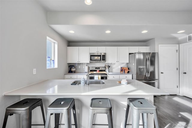 kitchen featuring a sink, stainless steel appliances, light countertops, white cabinetry, and a kitchen breakfast bar