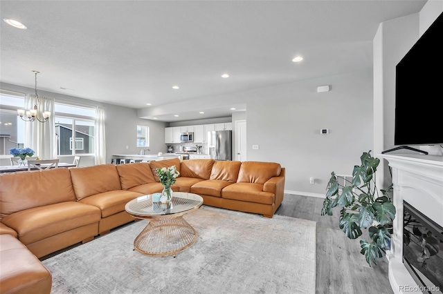 living room featuring a glass covered fireplace, recessed lighting, light wood-style floors, baseboards, and a chandelier