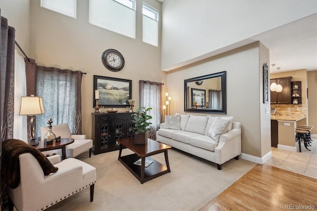 living room featuring light wood-style floors, a towering ceiling, and baseboards