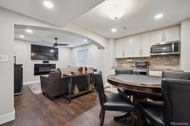 kitchen featuring arched walkways, stainless steel microwave, a glass covered fireplace, and white cabinetry