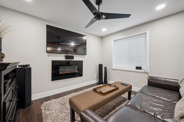 living room with a ceiling fan, a glass covered fireplace, dark wood finished floors, and baseboards