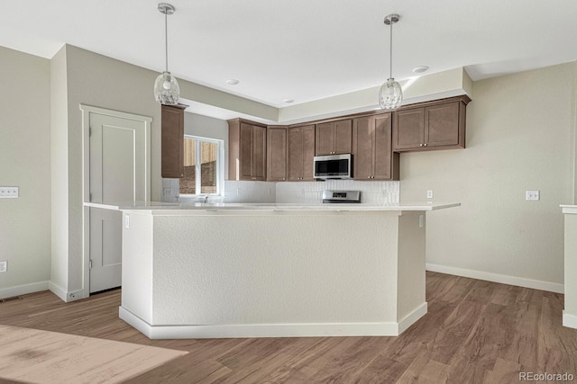 kitchen featuring a kitchen island, hanging light fixtures, stainless steel appliances, and light wood-type flooring