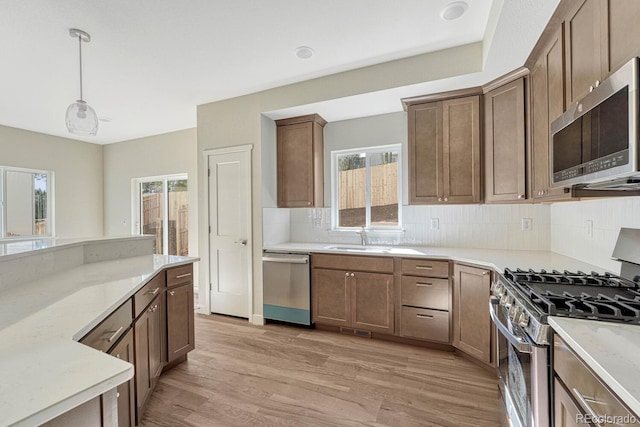 kitchen with light hardwood / wood-style flooring, sink, pendant lighting, appliances with stainless steel finishes, and tasteful backsplash