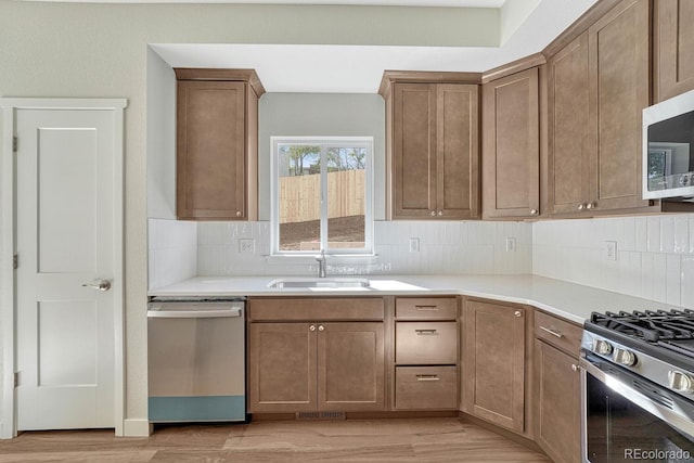 kitchen featuring appliances with stainless steel finishes, light hardwood / wood-style flooring, decorative backsplash, and sink