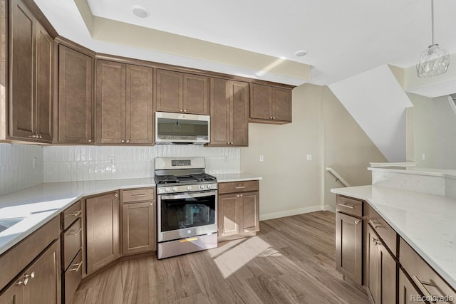 kitchen featuring decorative backsplash, appliances with stainless steel finishes, light stone countertops, light wood-type flooring, and decorative light fixtures