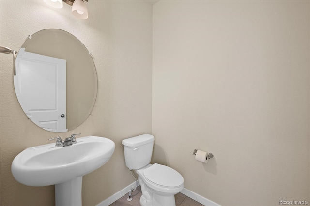 half bathroom with baseboards, a sink, toilet, and tile patterned floors