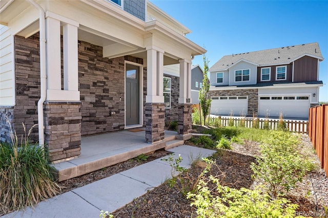 doorway to property featuring stone siding, a porch, an attached garage, and fence