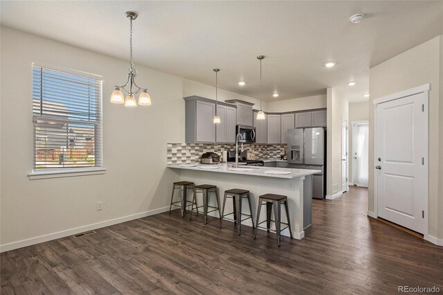 kitchen with kitchen peninsula, tasteful backsplash, dark hardwood / wood-style flooring, a breakfast bar area, and appliances with stainless steel finishes