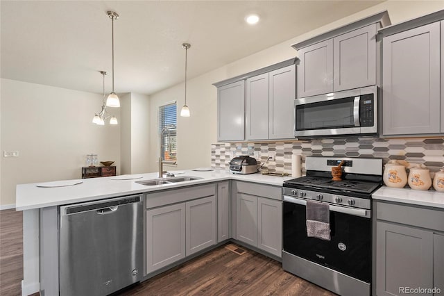 kitchen with appliances with stainless steel finishes, a peninsula, hanging light fixtures, light countertops, and gray cabinetry