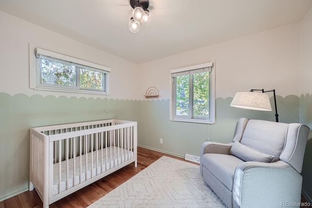 bedroom featuring multiple windows, wood-type flooring, and a crib