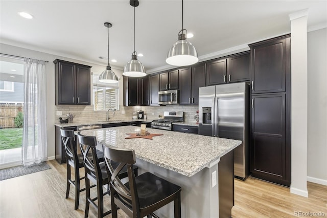 kitchen featuring a kitchen island, appliances with stainless steel finishes, pendant lighting, a kitchen bar, and dark brown cabinetry