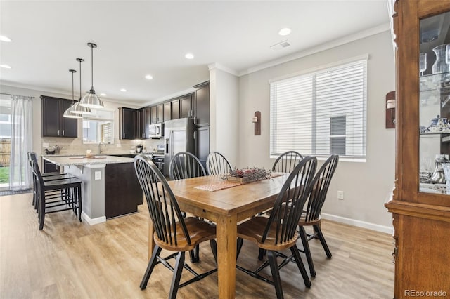 dining space with sink, crown molding, light hardwood / wood-style flooring, and plenty of natural light