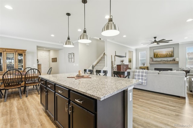 kitchen with a fireplace, a kitchen island, open floor plan, light stone countertops, and decorative light fixtures