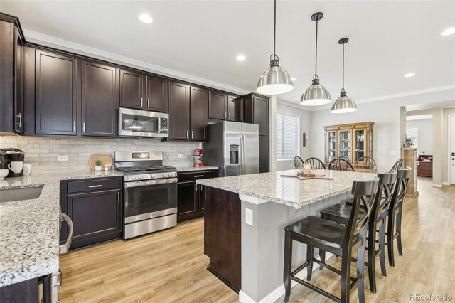 kitchen featuring a kitchen island, appliances with stainless steel finishes, a breakfast bar area, light stone countertops, and pendant lighting