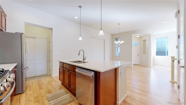 kitchen featuring a kitchen island with sink, hanging light fixtures, sink, light wood-type flooring, and appliances with stainless steel finishes