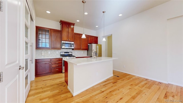 kitchen featuring backsplash, stainless steel appliances, a kitchen island with sink, light hardwood / wood-style flooring, and hanging light fixtures