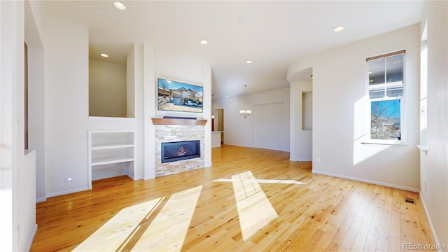 unfurnished living room with light hardwood / wood-style floors, a stone fireplace, and an inviting chandelier