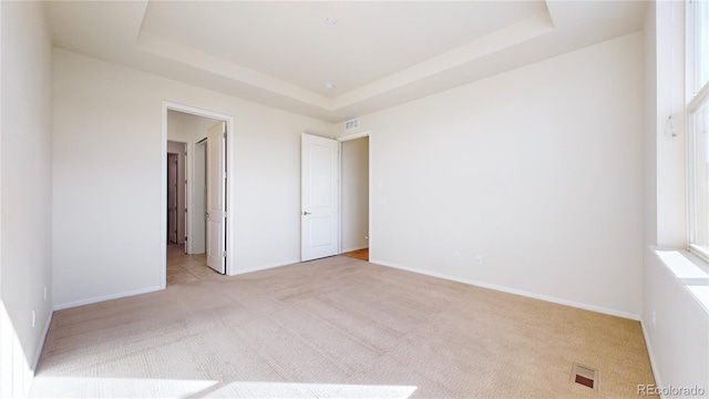 unfurnished bedroom with light carpet and a tray ceiling