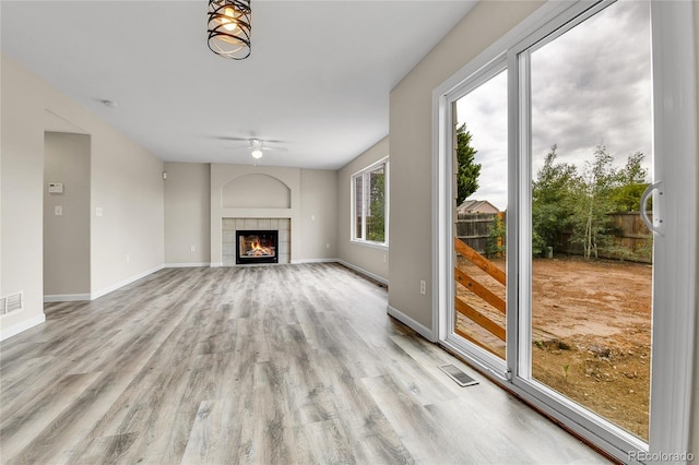22974 E Dorado Dr, Aurora, CO 80015 - unfurnished living room with light wood-style flooring, a ceiling fan, a tiled fireplace, and baseboards