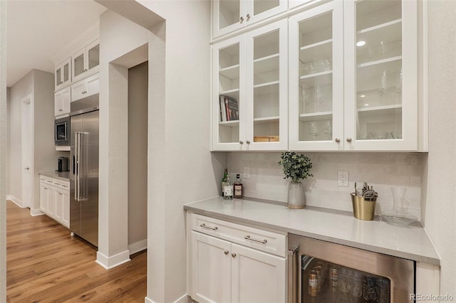 bar featuring backsplash, white cabinetry, light hardwood / wood-style floors, beverage cooler, and built in appliances