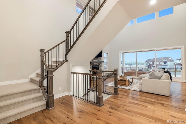 stairs with a towering ceiling, wood-type flooring, and a fireplace