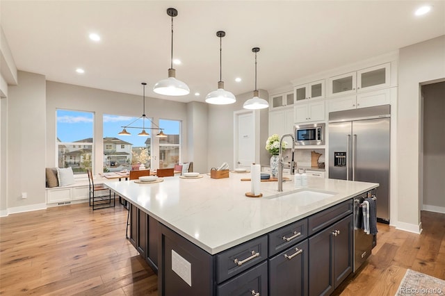 kitchen featuring white cabinets, decorative light fixtures, built in appliances, and an island with sink