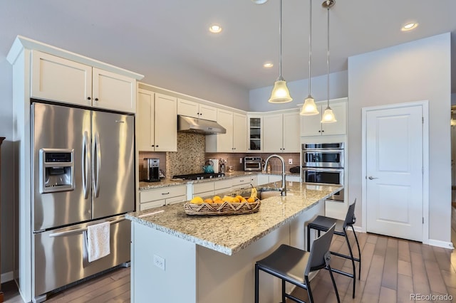15855 Wild Horse Dr, Broomfield, CO 80023 - kitchen with under cabinet range hood, stainless steel appliances, wood finished floors, decorative backsplash, and white cabinetry