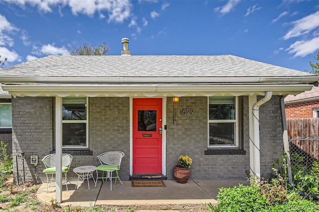 view of front of house featuring covered porch, roof with shingles, fence, and brick siding