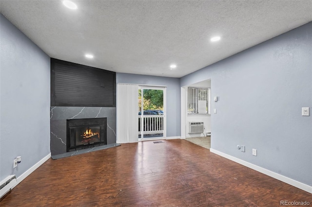 unfurnished living room with a textured ceiling, hardwood / wood-style flooring, an AC wall unit, a fireplace, and a baseboard radiator