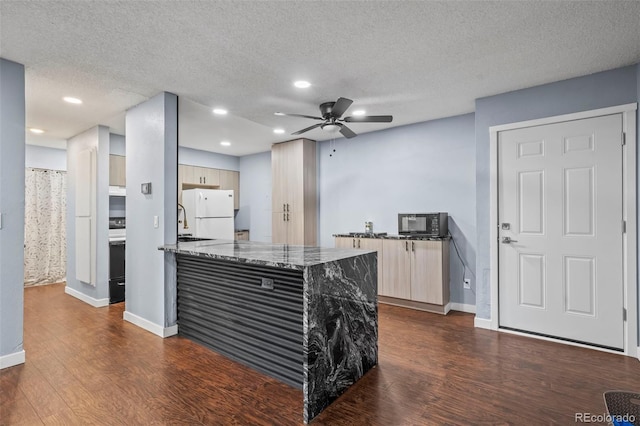 kitchen featuring ceiling fan, white refrigerator, a textured ceiling, dark stone countertops, and dark hardwood / wood-style flooring