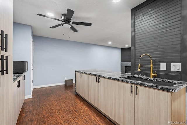 kitchen featuring light brown cabinetry, dark hardwood / wood-style floors, dark stone countertops, and ceiling fan