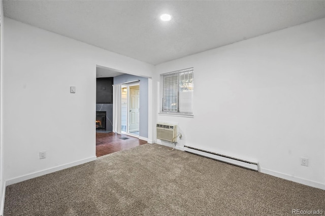 carpeted spare room featuring a large fireplace, a wall unit AC, and a baseboard radiator