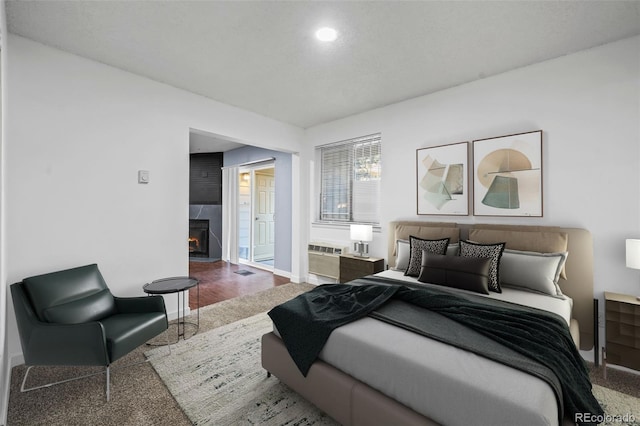 bedroom with wood-type flooring, a fireplace, and a wall mounted air conditioner