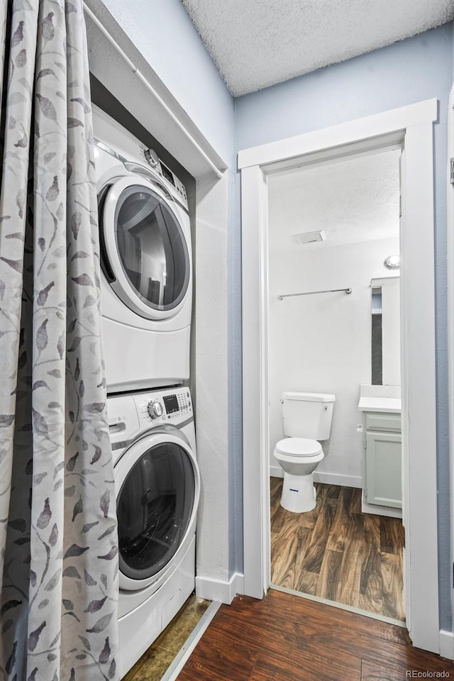 clothes washing area with a textured ceiling, dark hardwood / wood-style flooring, and stacked washing maching and dryer