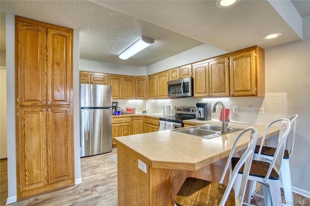 kitchen with stainless steel appliances, kitchen peninsula, light wood-type flooring, a kitchen bar, and sink