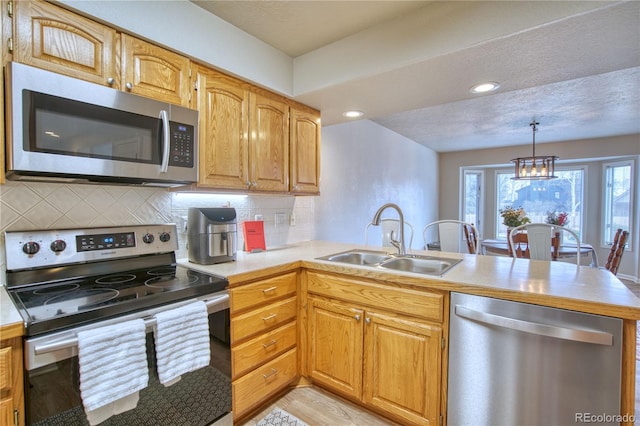 kitchen with pendant lighting, backsplash, kitchen peninsula, appliances with stainless steel finishes, and sink