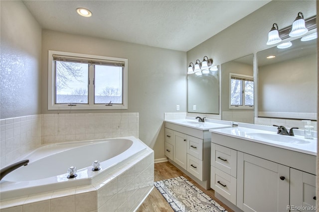 bathroom with a textured ceiling, hardwood / wood-style flooring, vanity, and a relaxing tiled tub