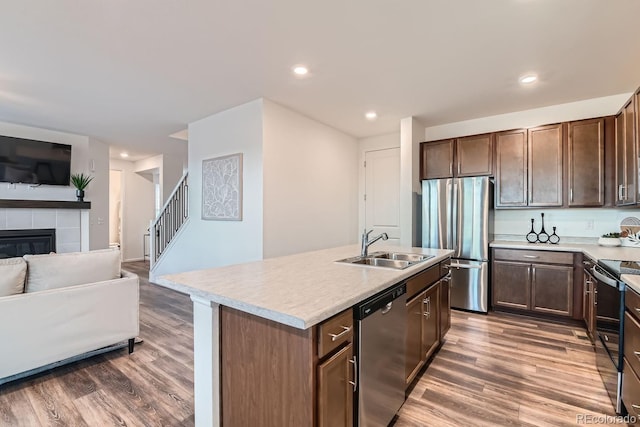 kitchen with a kitchen island with sink, a tile fireplace, sink, dark hardwood / wood-style floors, and stainless steel appliances