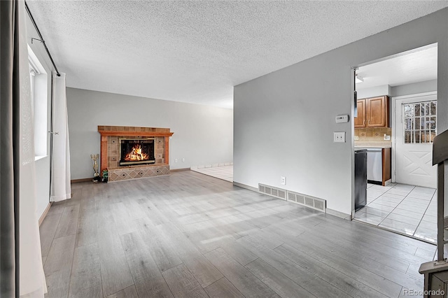 unfurnished living room with a tile fireplace, a textured ceiling, and light hardwood / wood-style floors