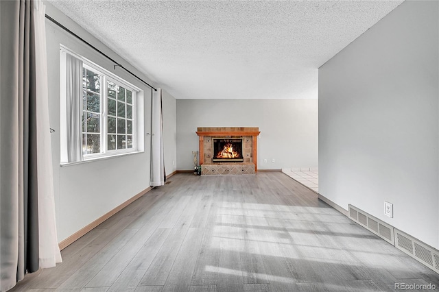 unfurnished living room featuring a textured ceiling, light wood-type flooring, and a fireplace