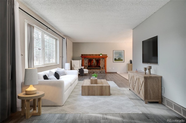 living room featuring a textured ceiling, light wood-type flooring, and a fireplace