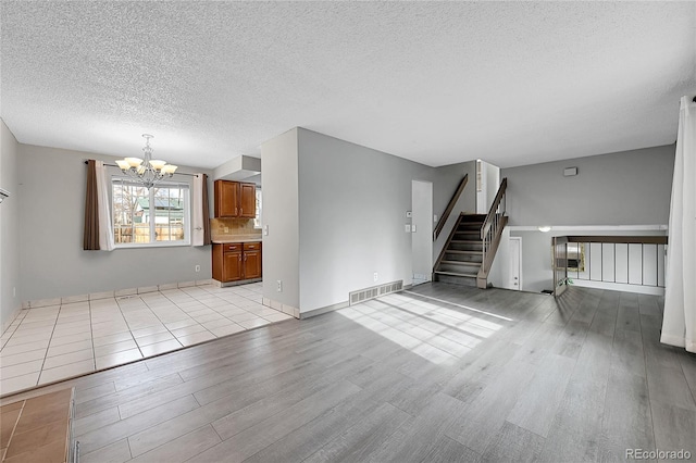 unfurnished living room with light wood-type flooring, a chandelier, and a textured ceiling