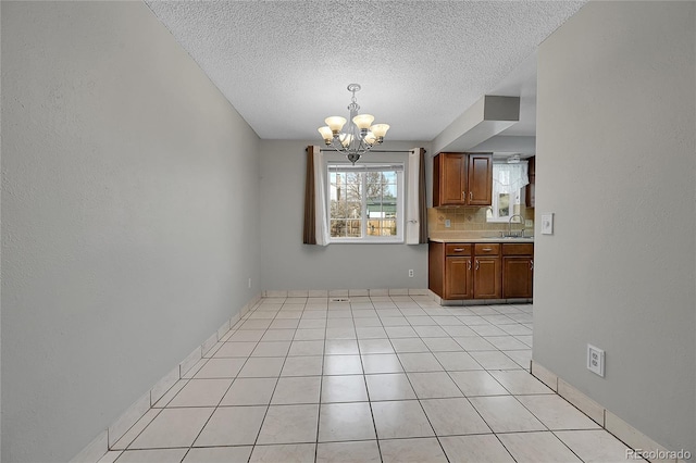 unfurnished dining area with light tile patterned floors, a notable chandelier, sink, and a textured ceiling