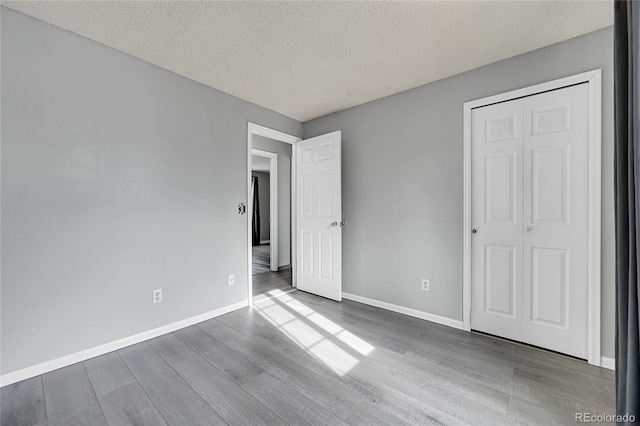 unfurnished bedroom with wood-type flooring, a closet, and a textured ceiling