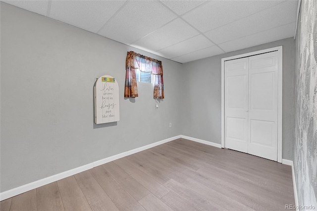 unfurnished bedroom with wood-type flooring, a paneled ceiling, and a closet