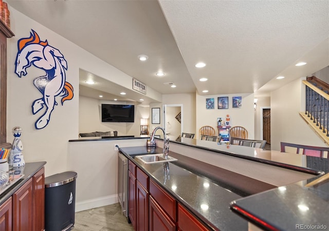 kitchen featuring a breakfast bar, dark stone counters, sink, kitchen peninsula, and light hardwood / wood-style flooring