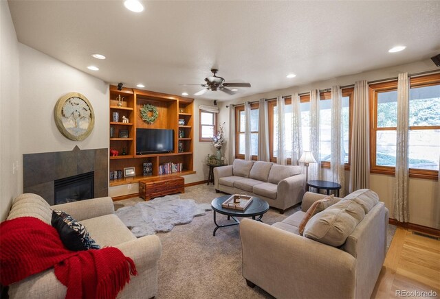 living room featuring ceiling fan, a tiled fireplace, and a healthy amount of sunlight