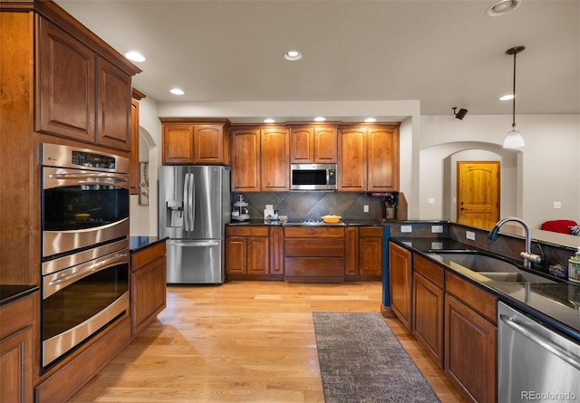 10215 W Wesley Dr, Lakewood, CO 80227 - kitchen featuring stainless steel appliances, arched walkways, a sink, pendant lighting, and brown cabinetry